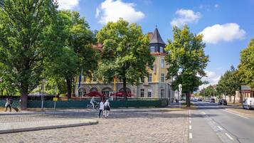 Ein Kopfsteinpflasterplatz mit einem historischen Gebäude mit einem Turm, umgeben von Bäumen und einem klaren Himmel.