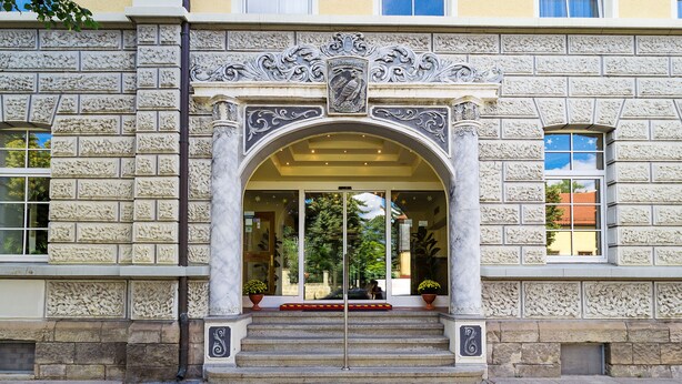 A building entrance with ornate stone carvings, a glass door, and steps leading up to it.