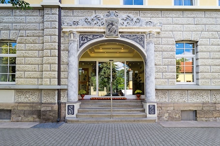 A building entrance with ornate stone carvings, a glass door, and steps leading up to it.