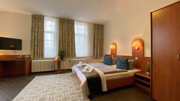 Une chambre d’hôtel avec un lit, des tables de chevet, un téléviseur, un radiateur et une fenêtre avec des rideaux.