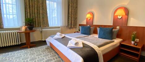 A hotel room with a large bed, two bedside lamps, a small table with a plant, and a radiator.