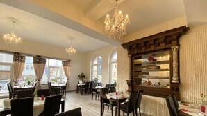 A restaurant with multiple tables, chandeliers, and a decorative column.