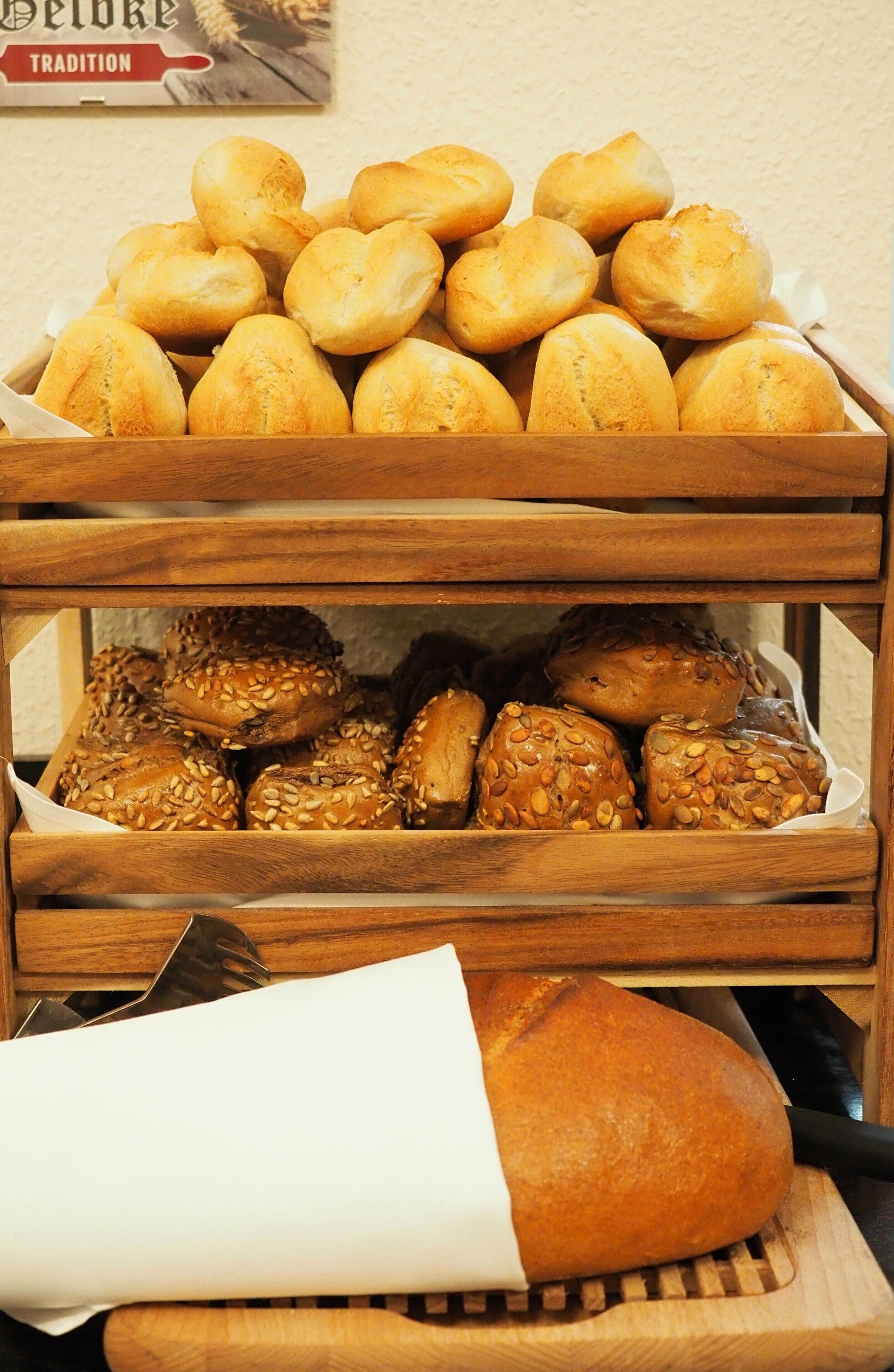 A wooden bread display with various types of bread, including rolls and seeded buns.