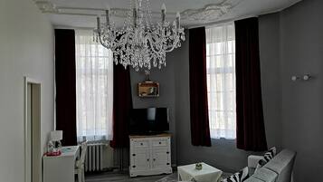 Una sala de estar con candelabro, televisor, sofá y aparador.