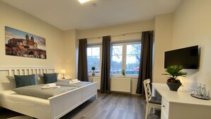 A hotel room with a bed, a desk, a chair, a TV, and a window with curtains.