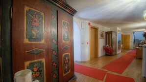 Un pasillo con puertas de madera, alfombra roja y una mesa con mantel floreado.