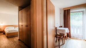 Habitación de hotel con armario de madera, una cama, una mesita con sillas y una ventana con cortinas.