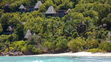A tropical resort with thatched-roof villas surrounded by dense greenery and a sandy beach.
