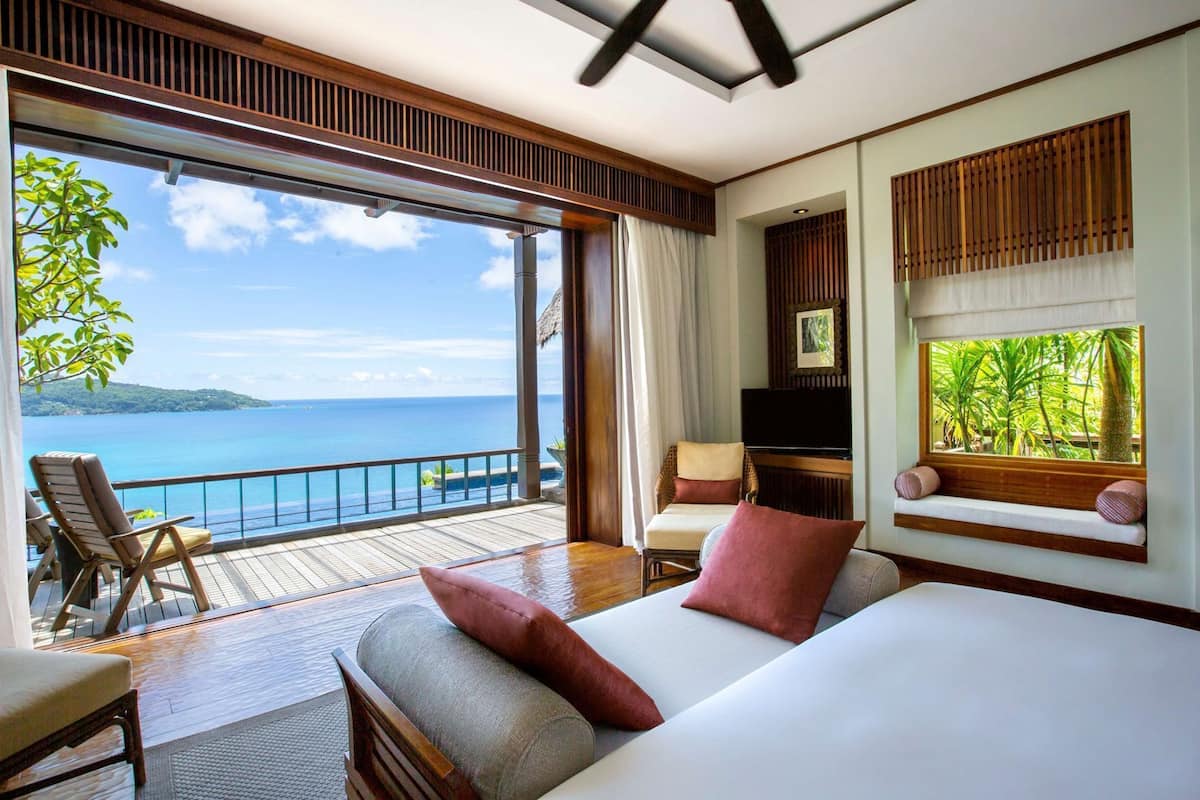 Une chambre dotée d’un grand lit, d’une télévision, d’un coin salon avec vue sur l’océan et d’un balcon avec une balustrade.