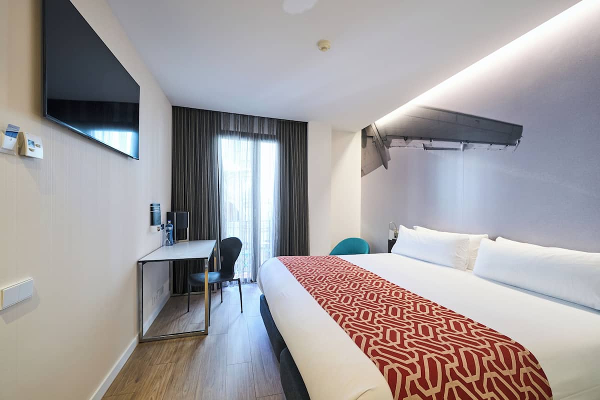 Een hotelkamer met een groot bed, een bureau met stoel, een flatscreen televisie aan de muur en een raam met gordijnen.