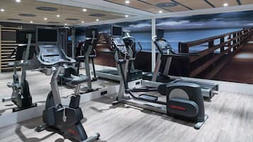 Een fitnessruimte met diverse cardioapparaten, een houten terras en een prachtig uitzicht op de oceaan.