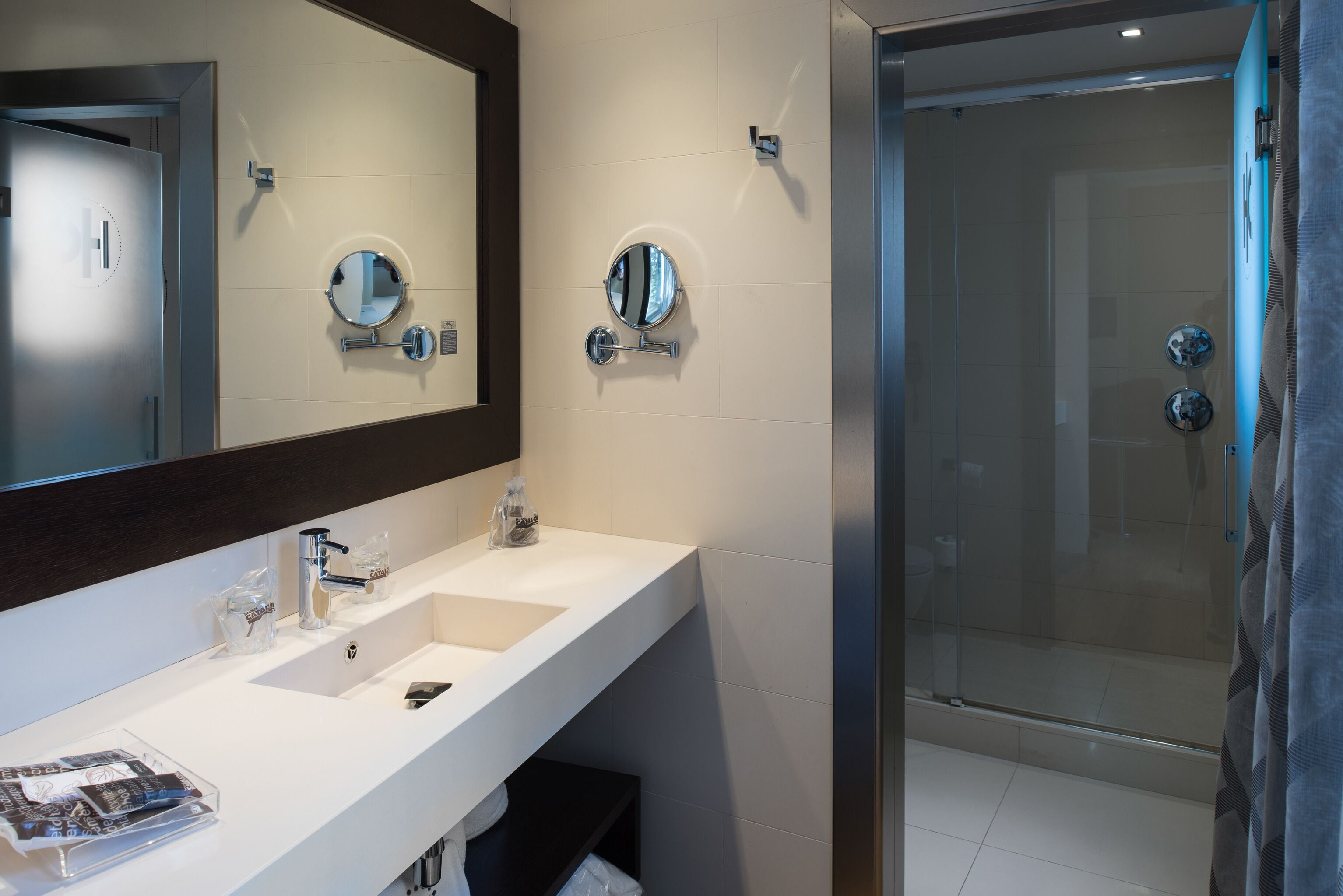 A modern bathroom with a large mirror, two sinks, a shower, and a glass-enclosed shower area.