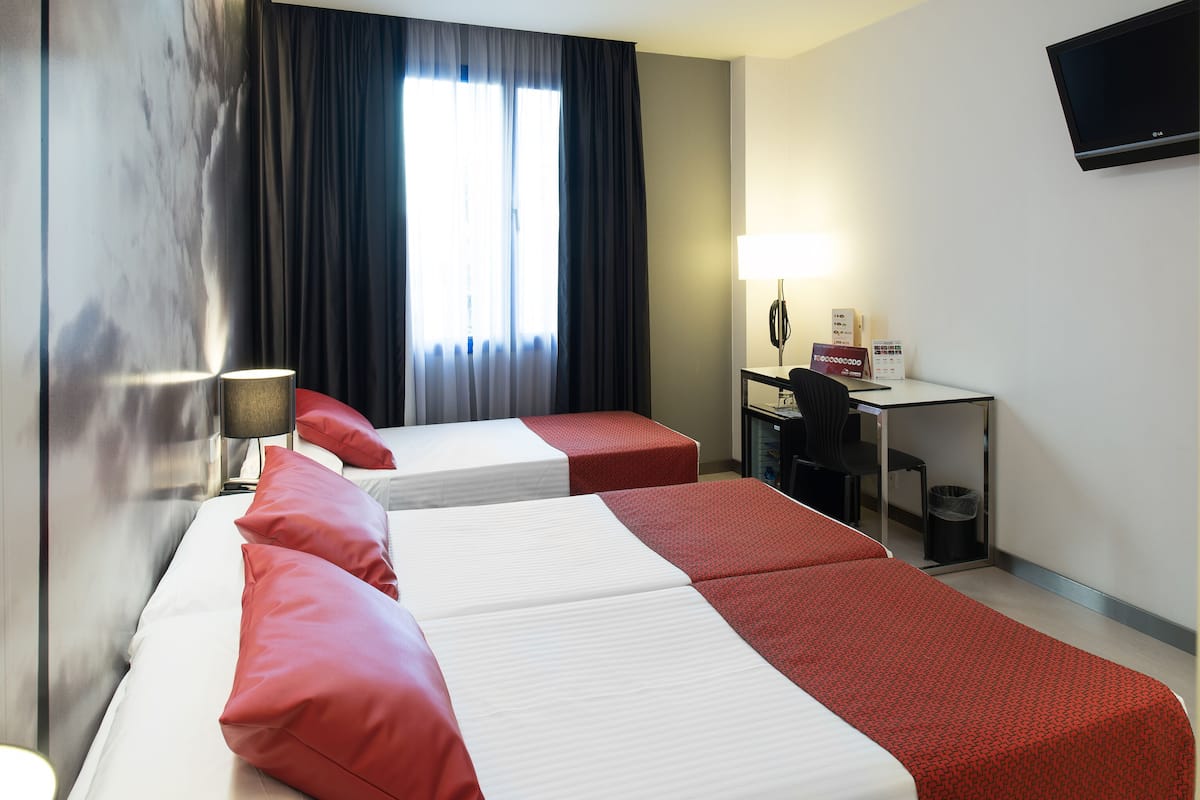 Hotelkamer met twee bedden, een bureau, een stoel, een televisie en een raam met gordijnen.