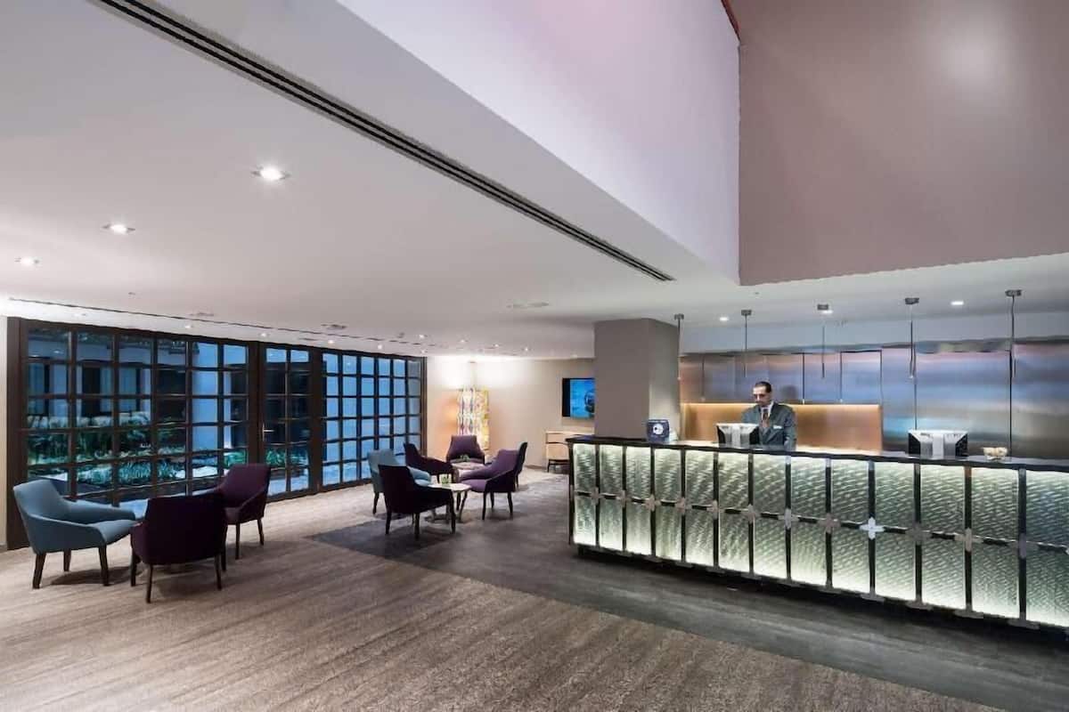 A modern hotel lobby with a reception desk, seating area, and large windows.