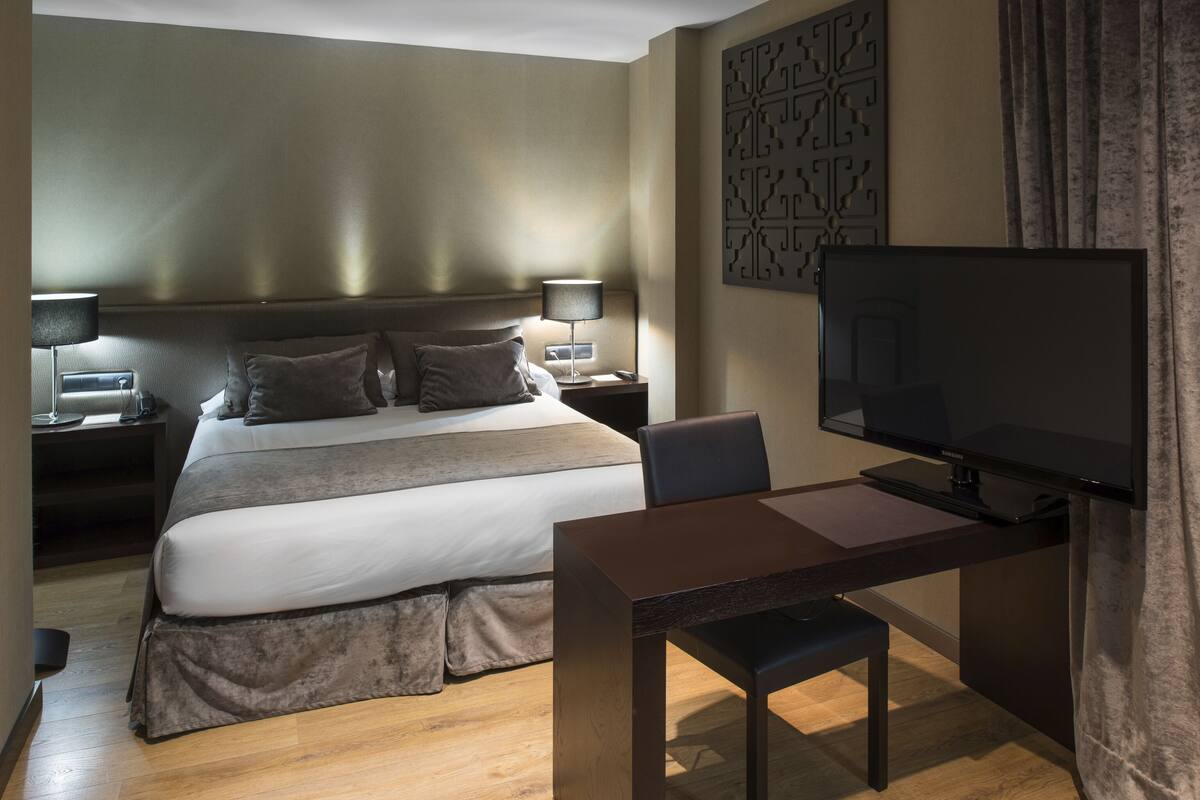 Een moderne hotelkamer met een groot bed, nachtkastjes met lampen, een flatscreen televisie en een houten bureau met een stoel.