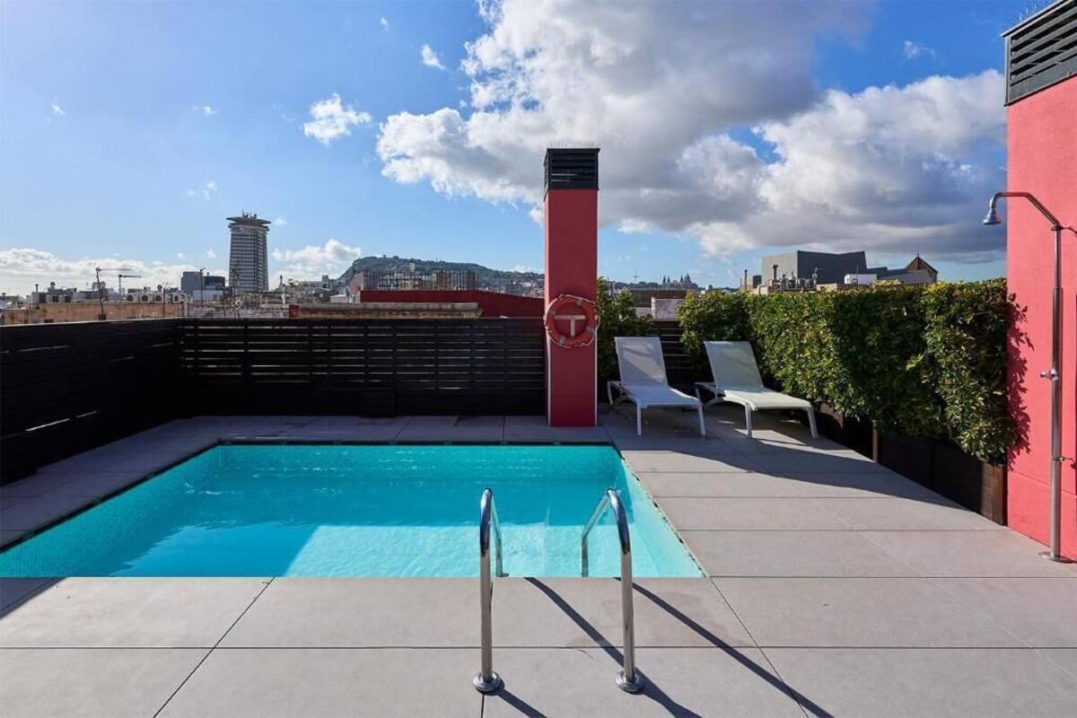 A rooftop pool with a city view, a red pillar, and lounge chairs.