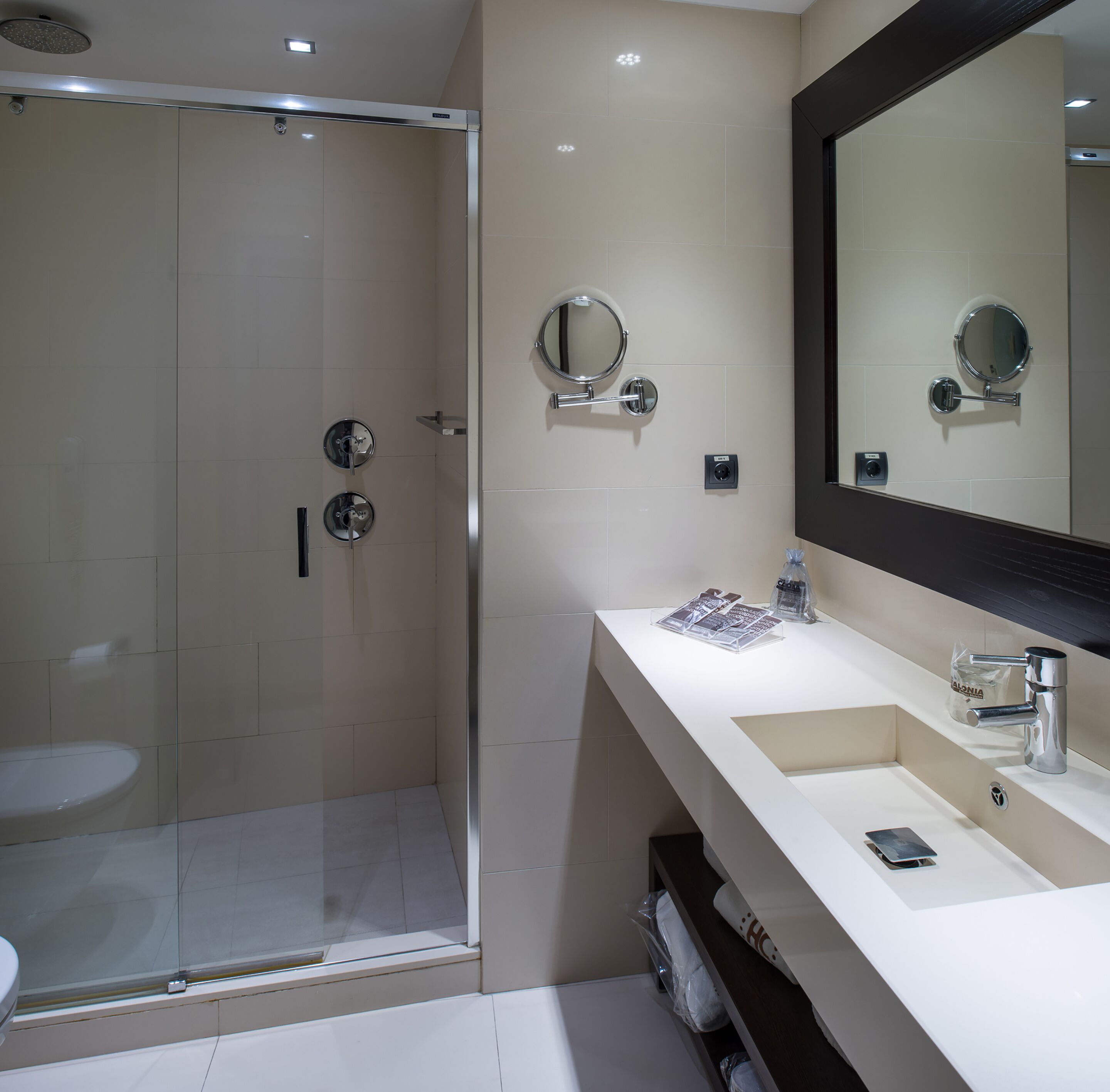 A modern bathroom with a glass-enclosed shower, a large mirror, and a white vanity with a sink and a handheld showerhead.