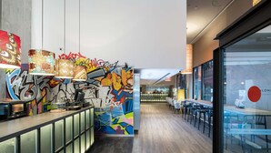 A modern hotel lobby with a long reception desk, colorful graffiti art on the walls, and a seating area with tables and chairs. - Catalonia Avinyó (Barcelona)