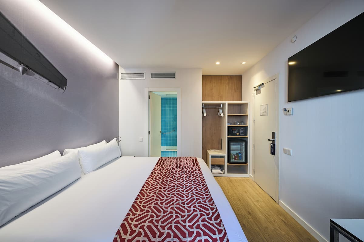 Een moderne hotelkamer met een groot bed, een televisie, een kledingkast en een badkamer die door een geopende deur zichtbaar is.