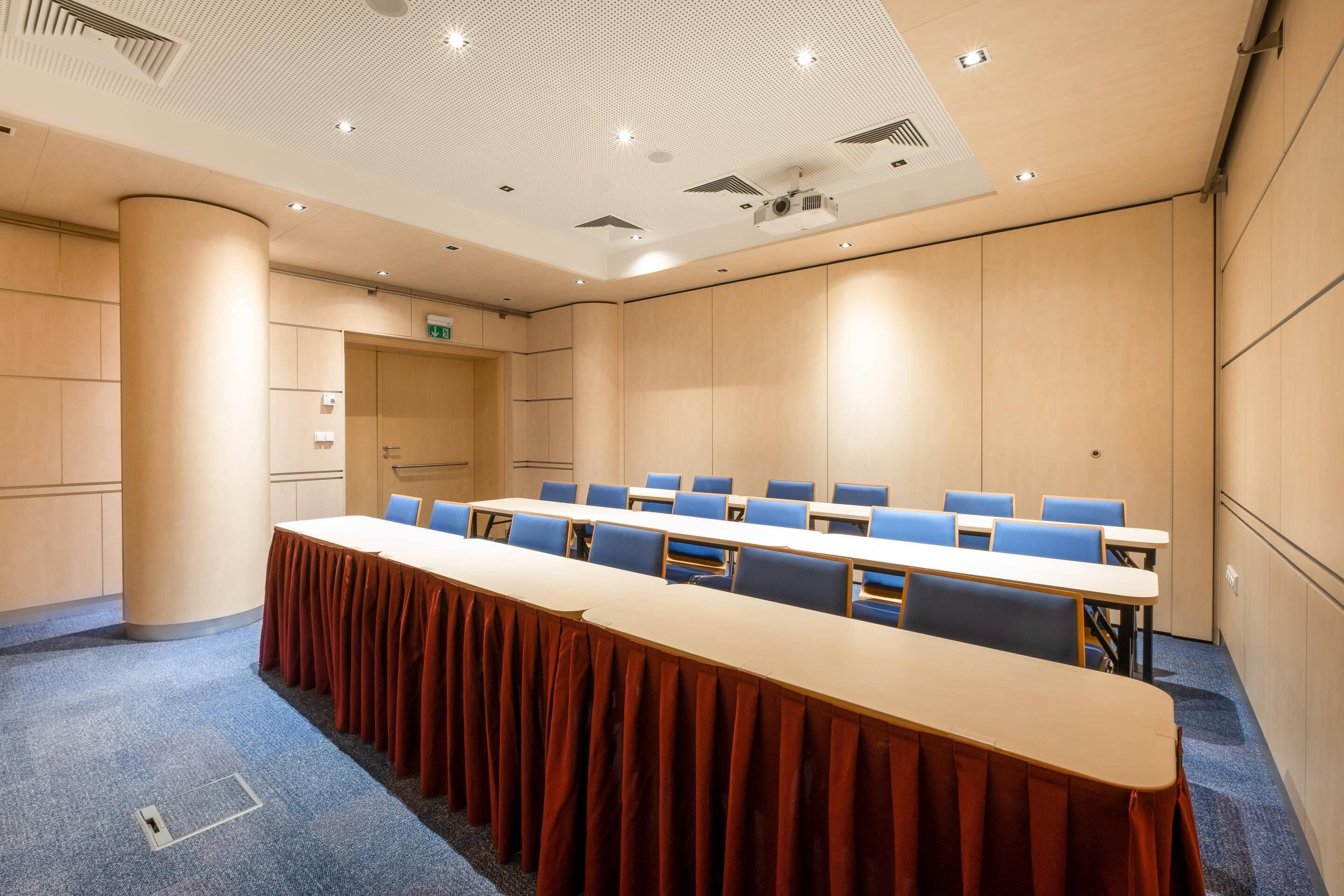 A conference room with a long table, blue chairs, and a carpeted floor.
