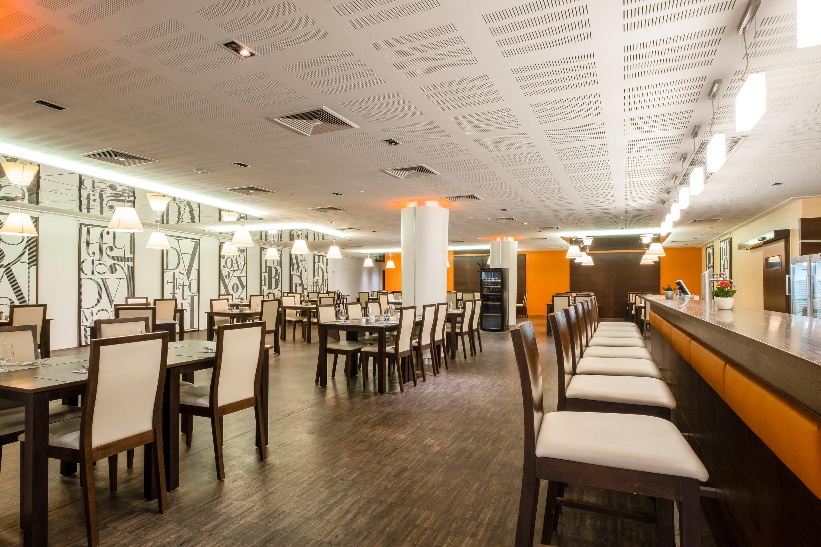 A restaurant with multiple dining tables and chairs, a bar area, and a ceiling with a grid pattern.
