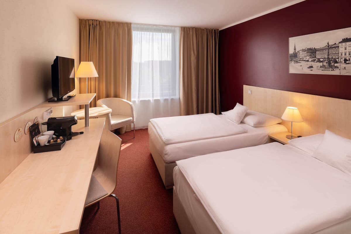 Quarto de hotel com duas camas, uma mesa com cafeteira, televisão e um quadro na parede.