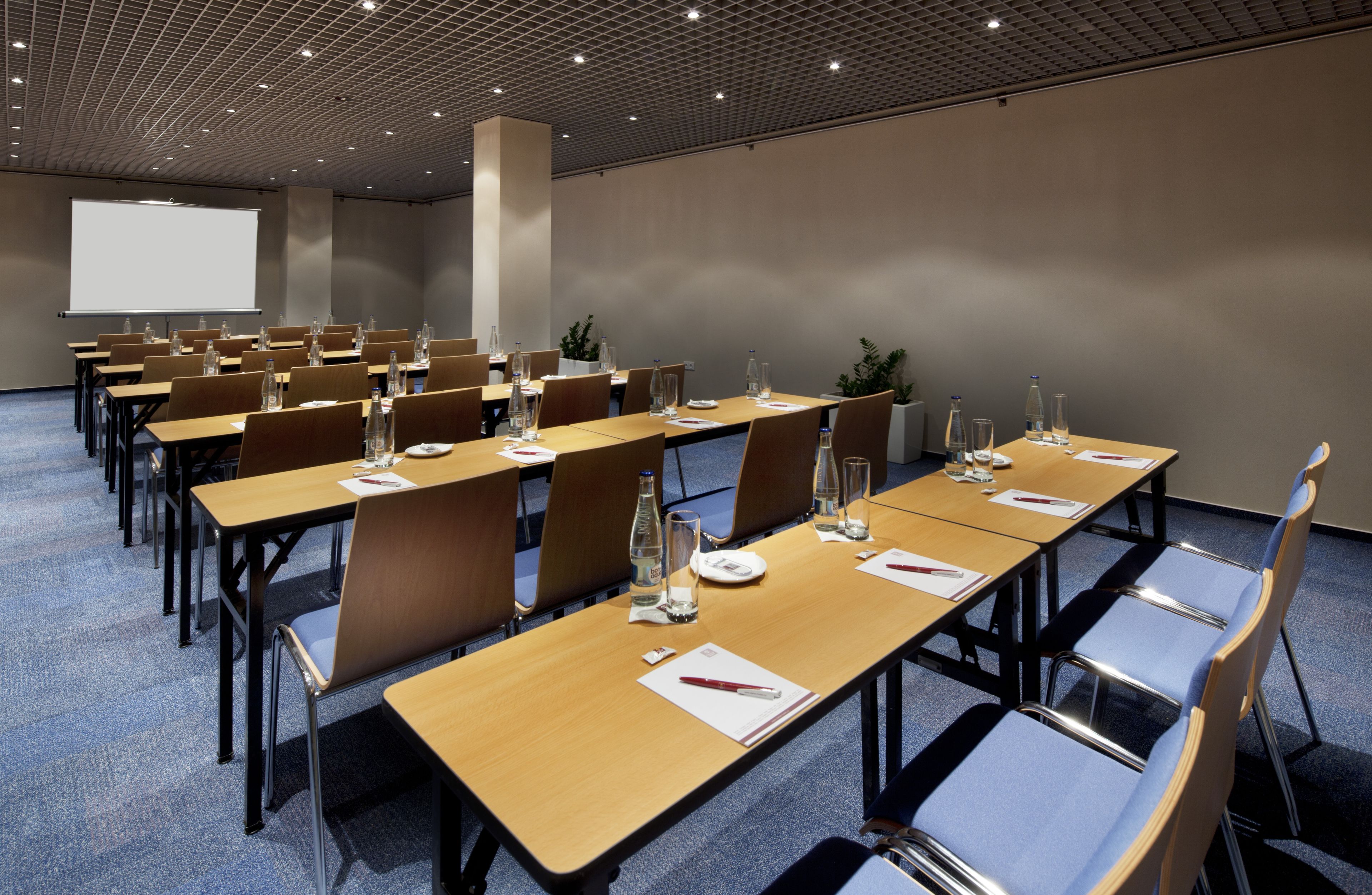 Ein Konferenzraum mit mehreren Tischen, Stühlen und einer Projektionsleinwand.