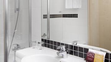 A bathroom with a glass shower enclosure, a white sink with a chrome faucet, and a mirror above the sink.