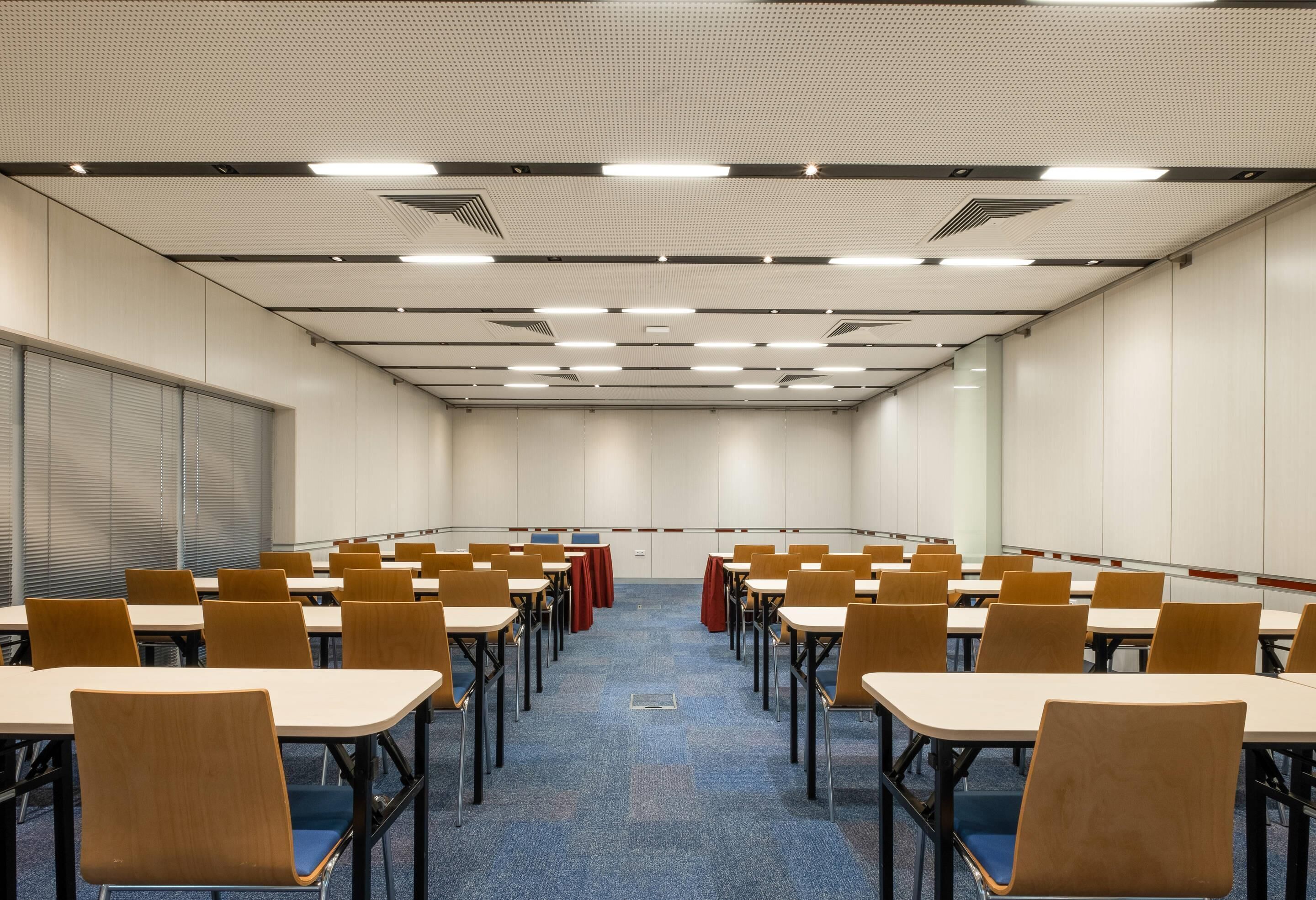 Ein Konferenzraum mit Tischen und Stühlen, einem Teppichboden und einer abgehängten Deckenbeleuchtung.