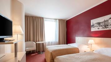 A hotel room with two beds, a desk with a TV, a chair, a small table, and a window with curtains.