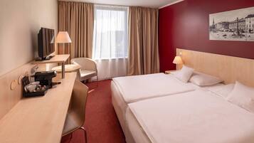 Een hotelkamer met een bureau, twee bedden, een stoel, een televisie en een raam met gordijnen.
