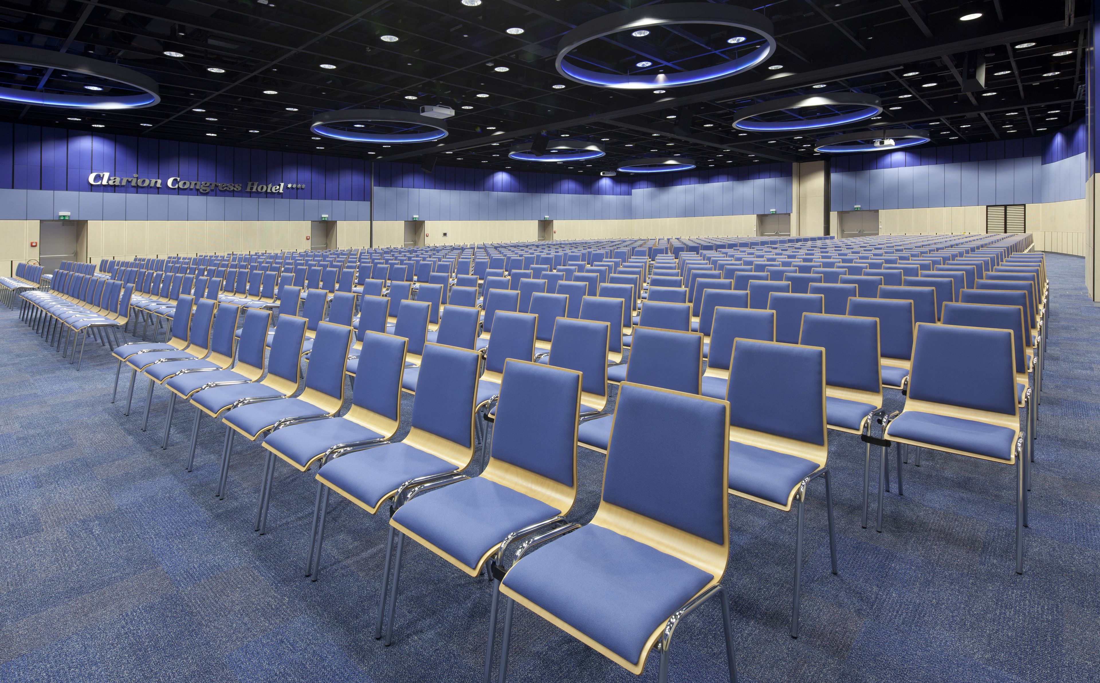 Une salle de conférence avec des rangées de chaises bleues et une scène à l’avant.