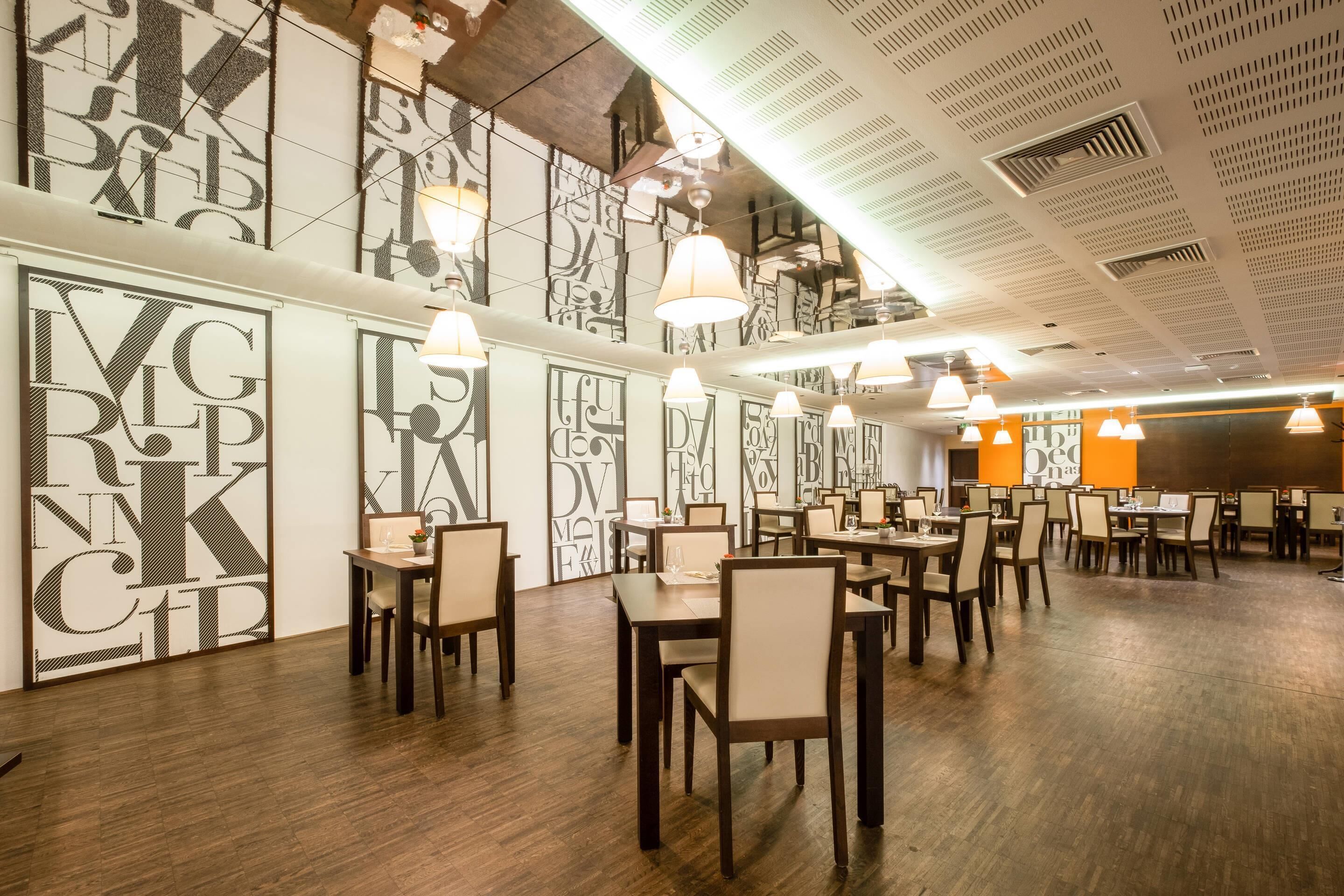 Un restaurante con una decoración moderna, que incluye arte mural geométrico, mesas de madera e iluminación colgante.