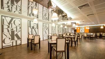 Un restaurante con una decoración moderna, que incluye arte mural geométrico, mesas de madera e iluminación colgante.