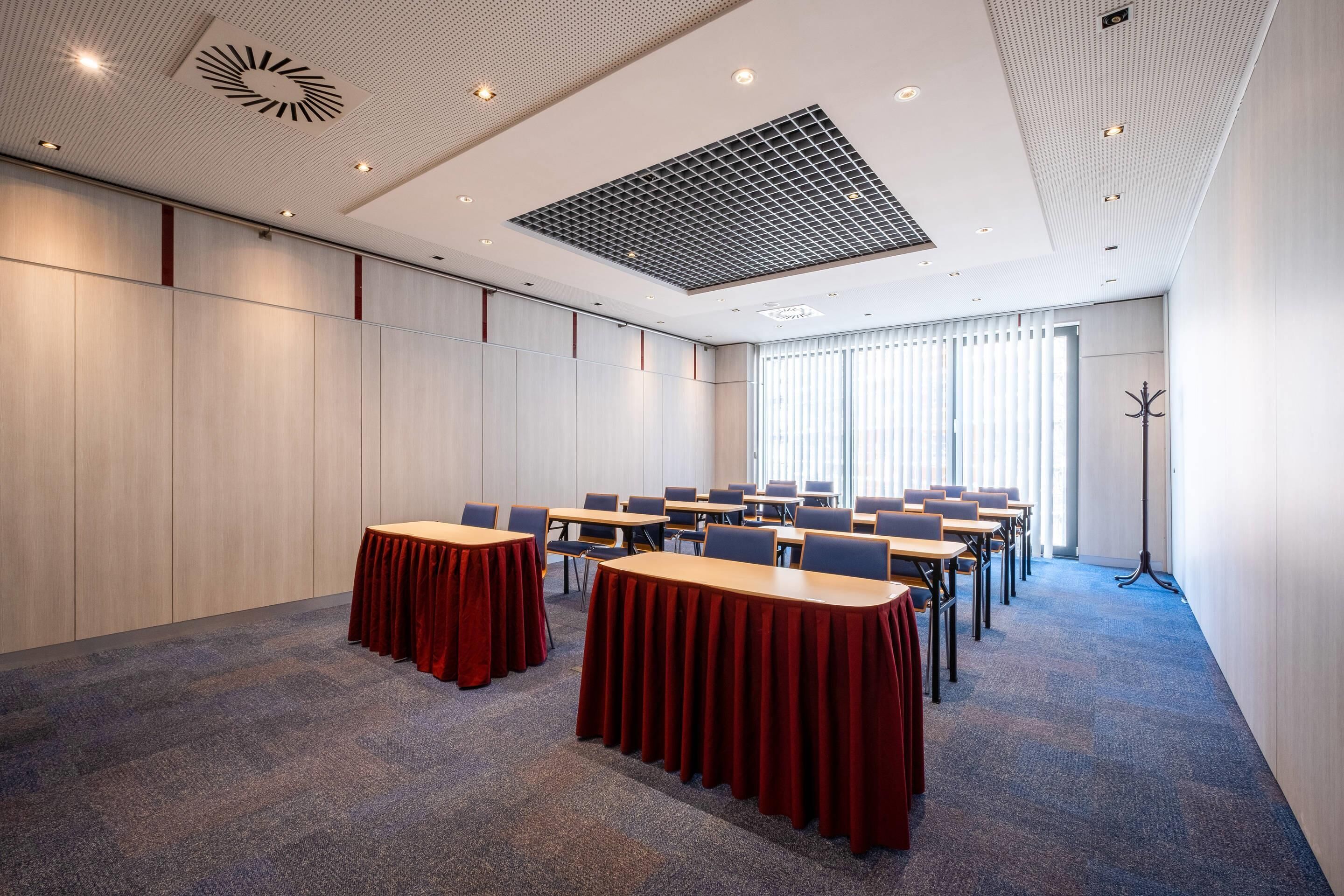 Un salón de conferencias con mesas, sillas y un ventanal con persianas.