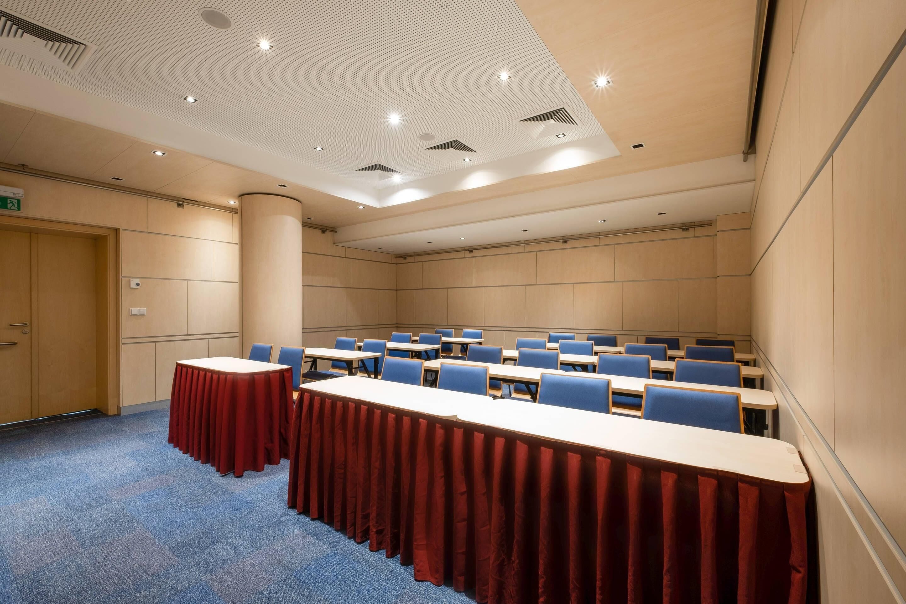 Une salle de conférence avec une longue table, des chaises bleues et une nappe rouge.