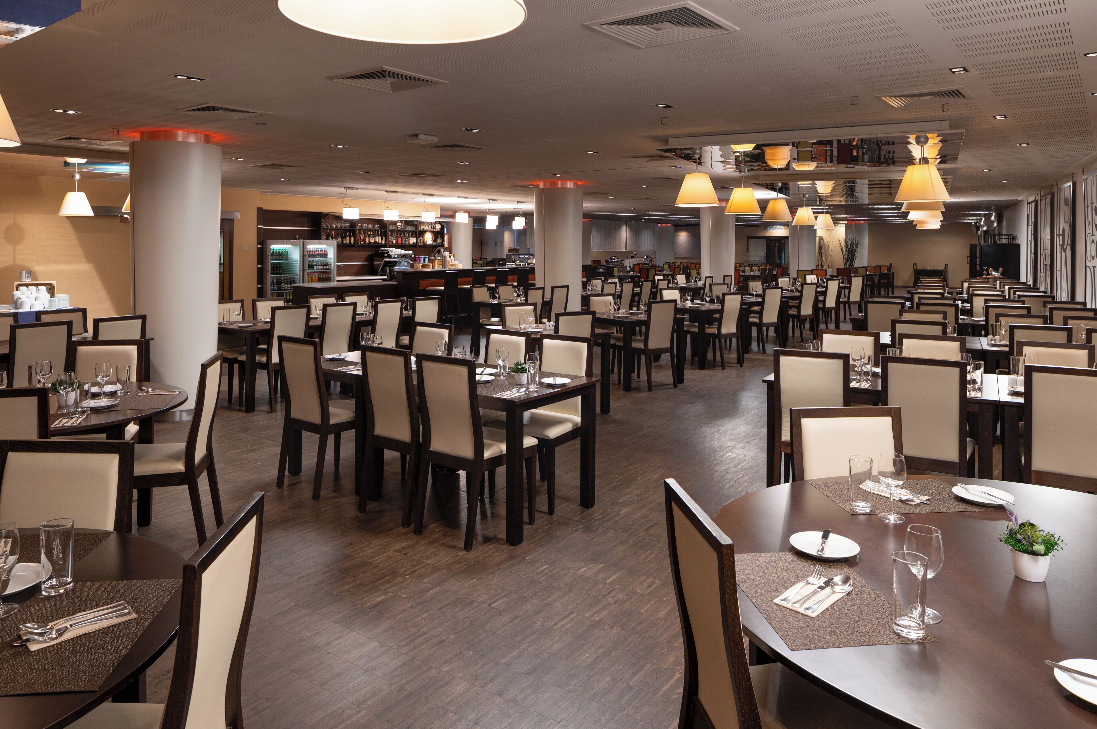 Ein geräumiges Restaurant mit mehreren Tischen, Stühlen, einer Bar und Pendelleuchten.