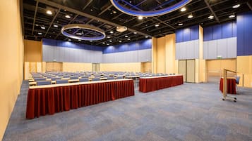 A conference room with rows of tables, a podium, and a carpeted floor.