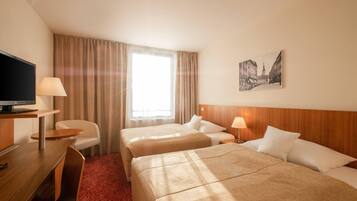 Een hotelkamer met twee bedden, een bureau met een televisie, een stoel, een lamp en een lijst aan de muur.