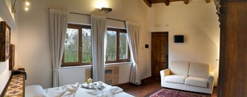 Una habitación con una cama, un sofá blanco y un amplio ventanal con cortinas.