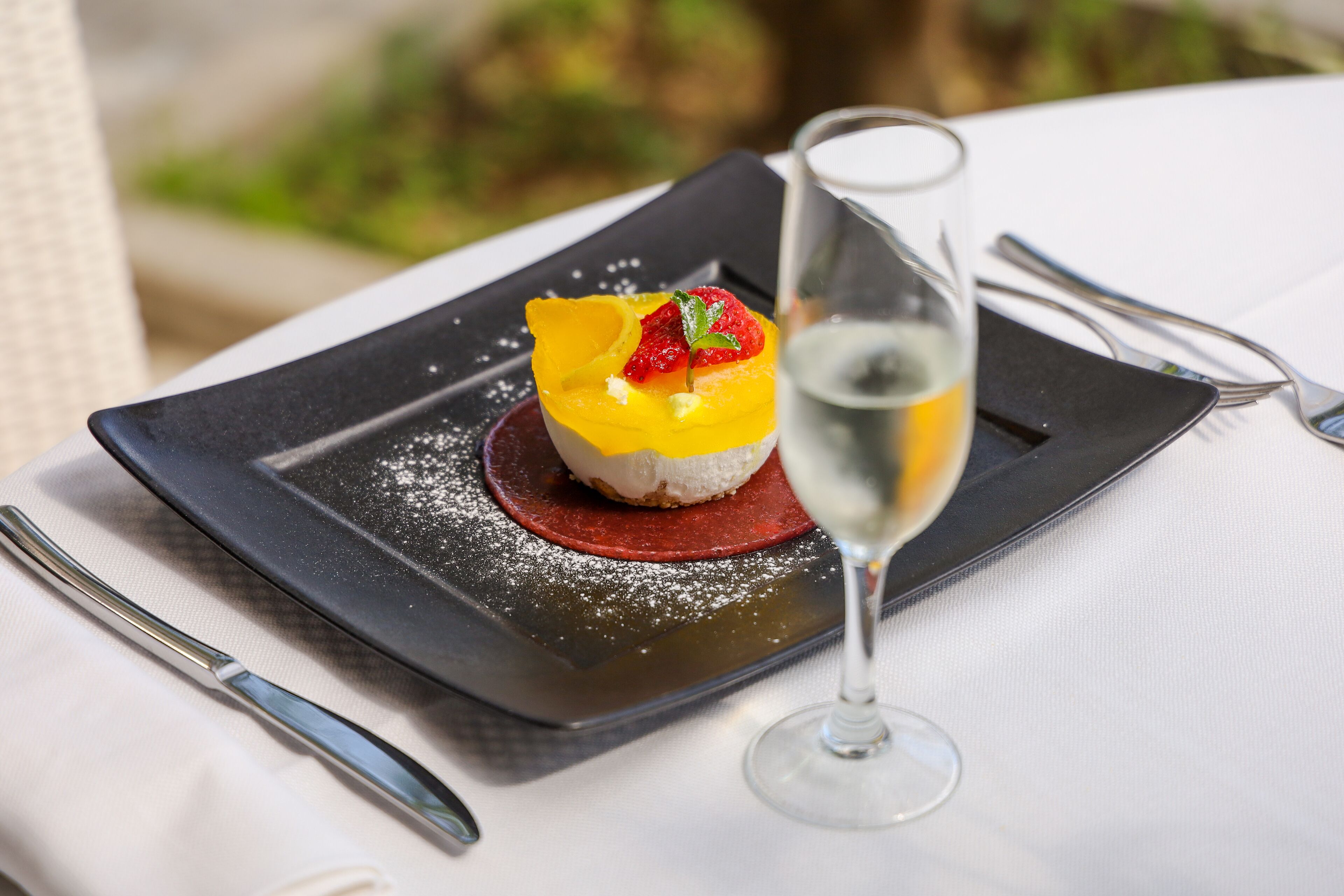 Un dessert servi dans une assiette carrée, accompagné d’un verre de vin blanc.