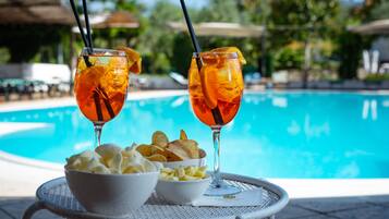 A poolside setting with two drinks in glasses, a bowl of chips, and a bowl of dip.