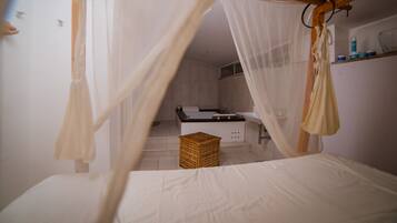 A bedroom with a canopy bed, a small wooden stool, and a visible bathroom with a bathtub and sink.