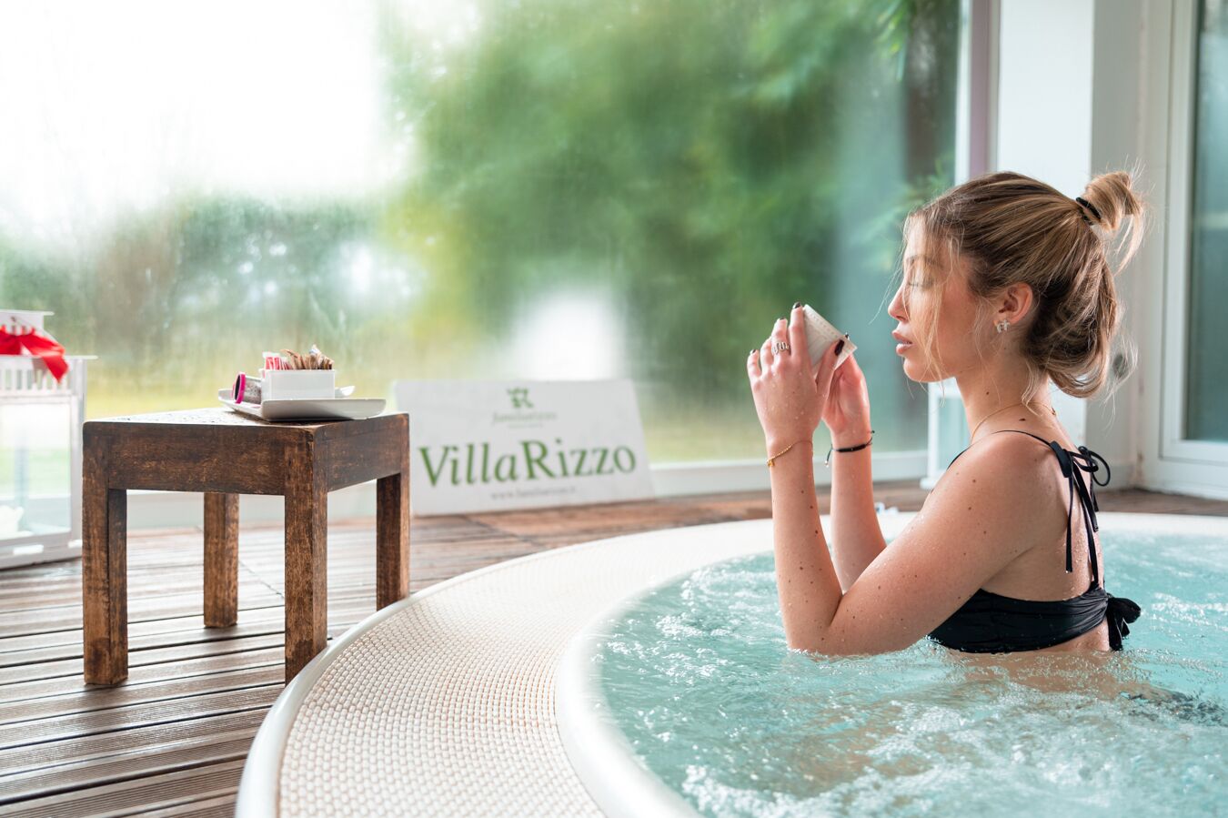 A woman in a hot tub with a sign reading "VillaRizzo" in the background.