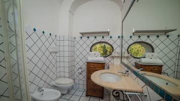 A bathroom with a bidet, toilet, sink, and two wooden cabinets with mirrors.