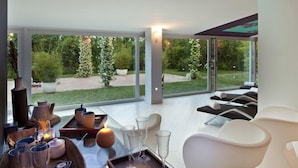 A modern living room with a glass table, white sofas, and a view of a garden through large windows. - Hotel Villa Rizzo Resort & Spa (San Cipriano Picentino)