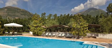 A swimming pool with lounge chairs and umbrellas, surrounded by trees and mountains.