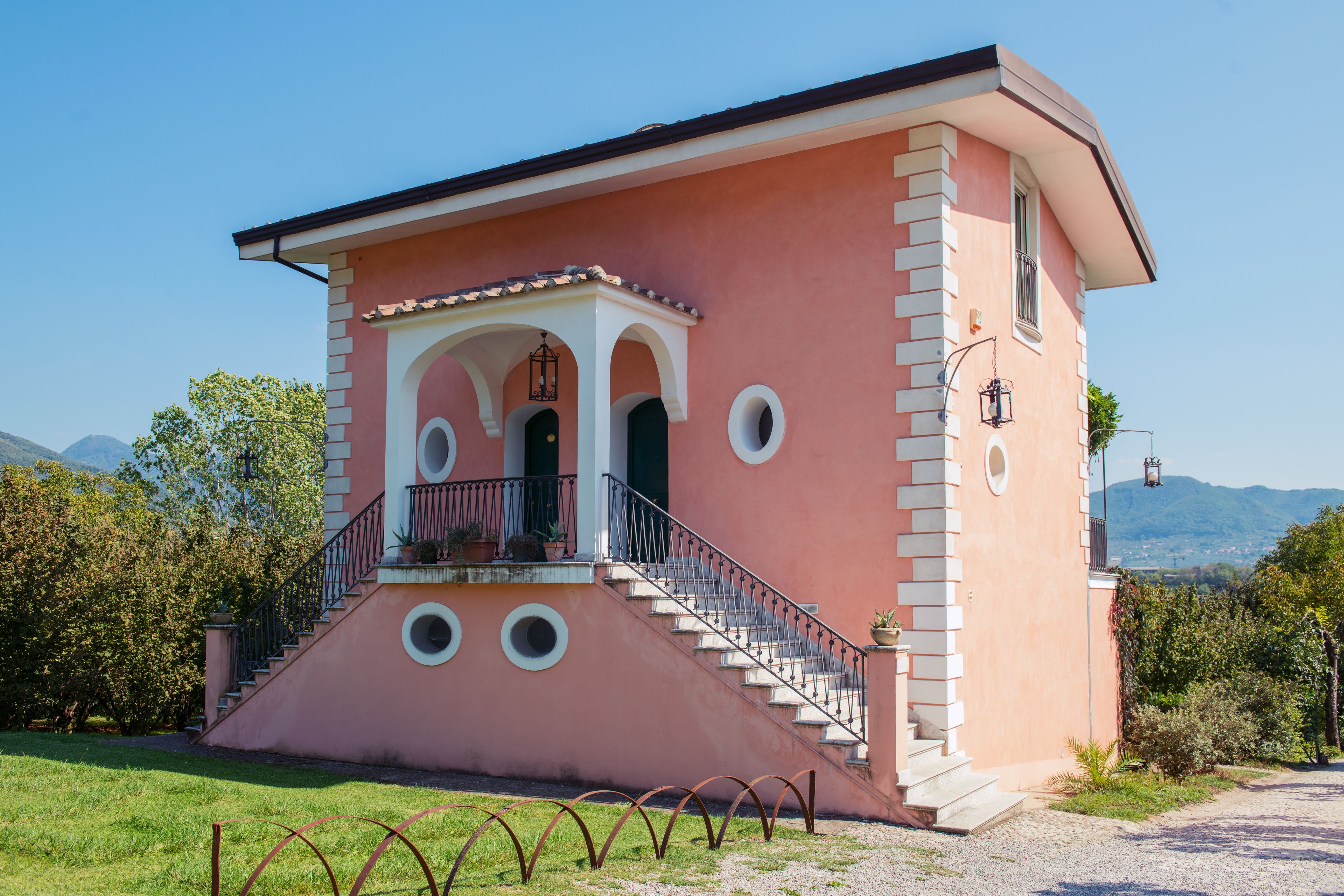 A pink building with a balcony, stairs, and a view of the mountains.