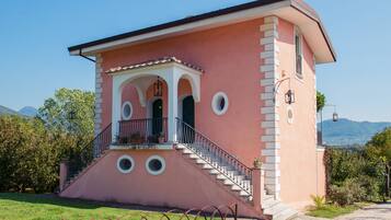 A pink building with a balcony, stairs, and a view of the mountains.