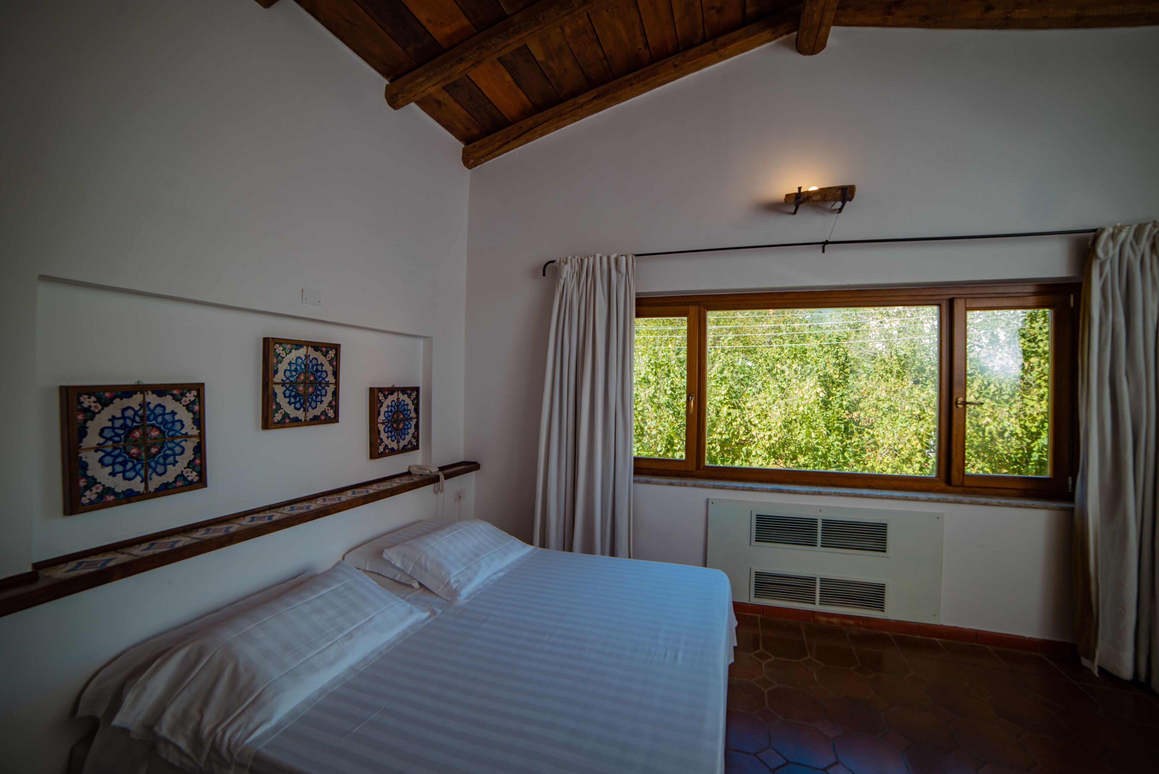 A bedroom with a bed, a window with curtains, and three wall-mounted decorative plates.